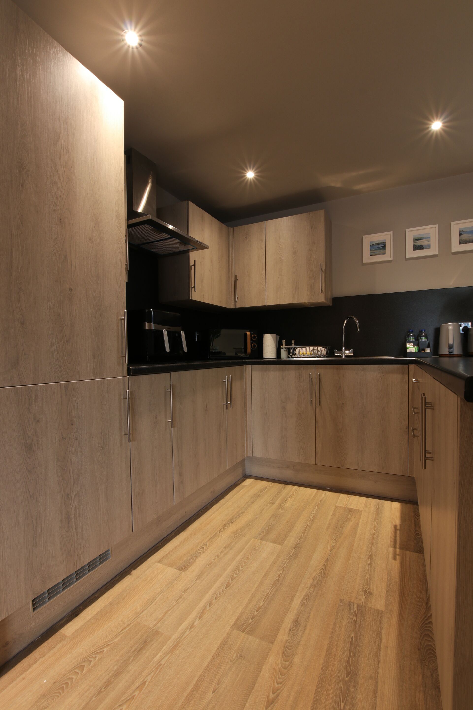 A modern kitchen with wooden cabinets, a black countertop, and a stainless steel range hood.
