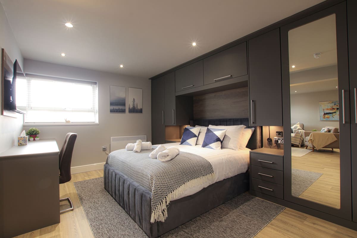 A modern bedroom with a large bed, bedside tables, a desk, and a wardrobe.