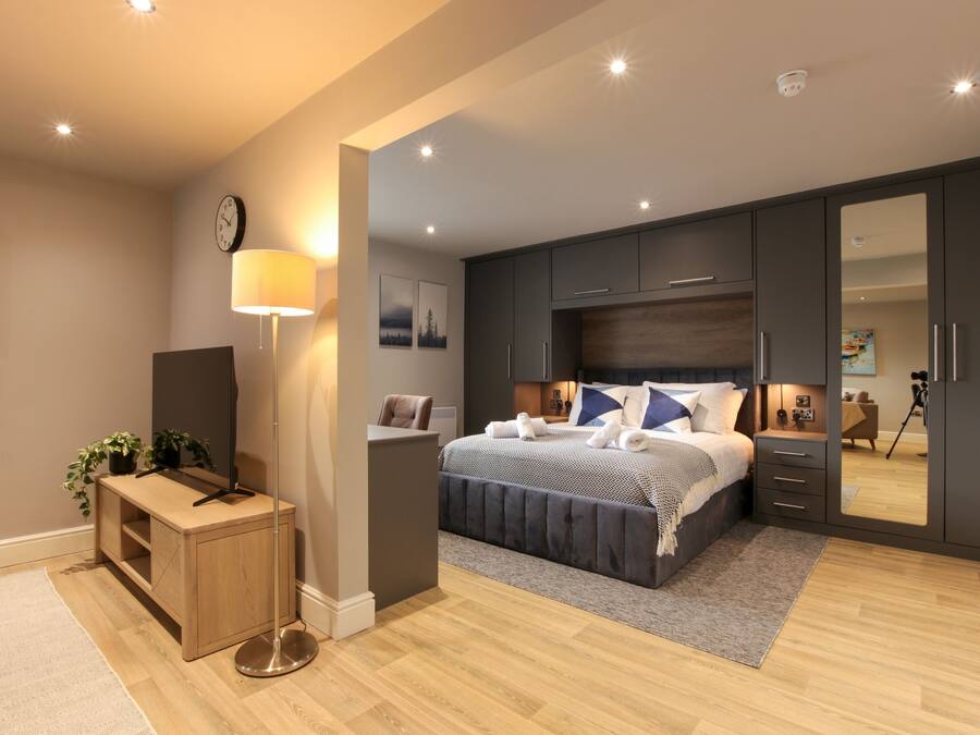 A modern bedroom with a large bed, a desk, a mirror, and a wardrobe.