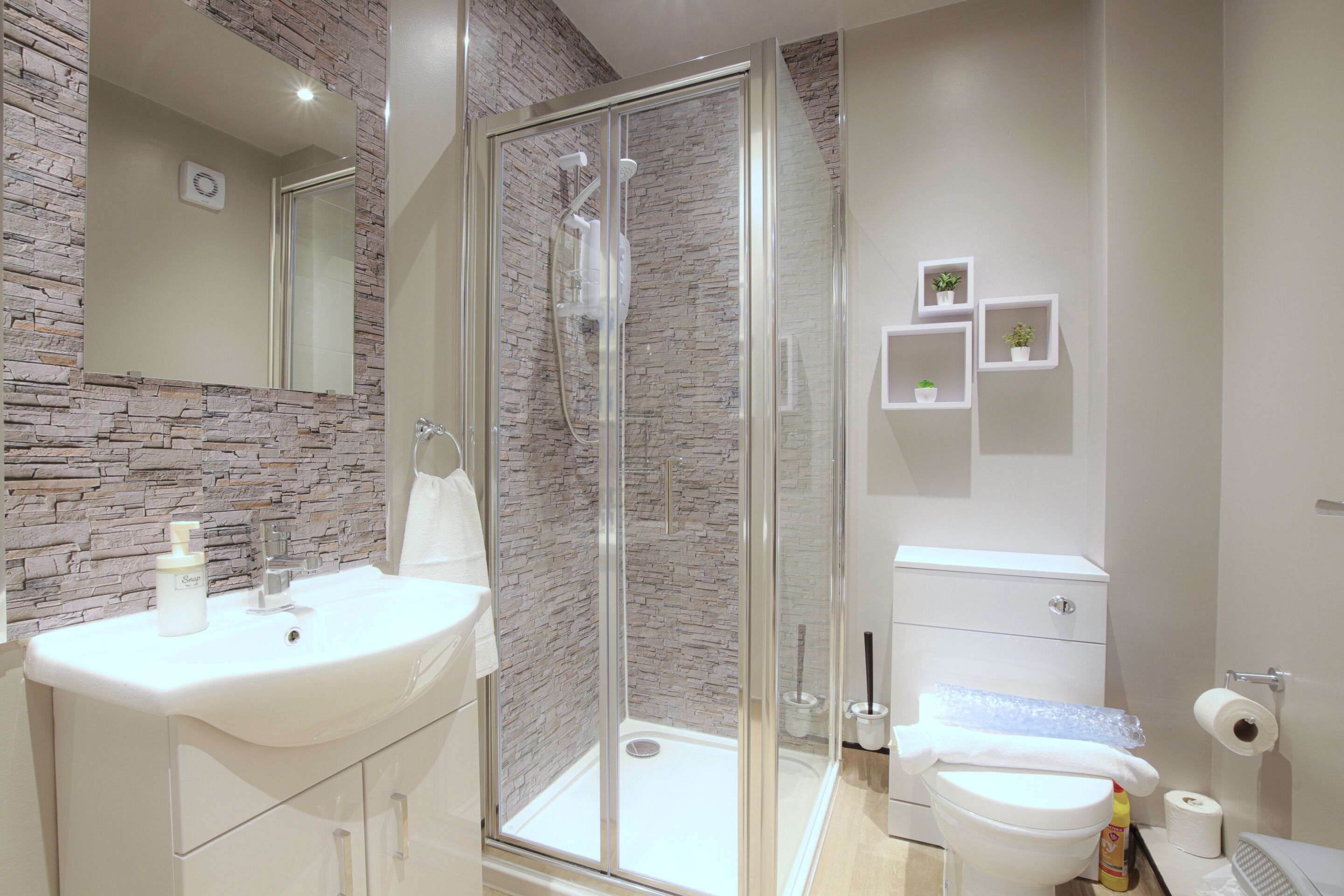 Ein modernes Badezimmer mit einer Steinwand, einer Duschkabine aus Glas, einem weißen Waschbecken und einer Toilette.