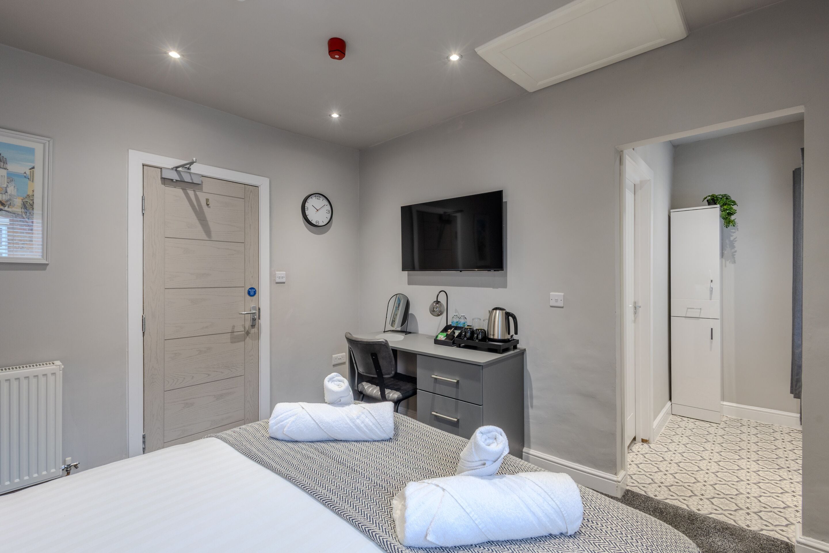 Una habitación de hotel con cama, escritorio, televisor, reloj y radiador.