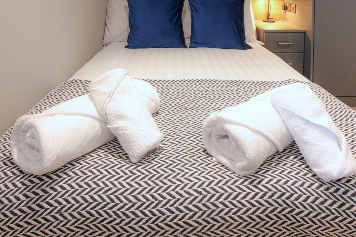 A neatly made bed with a patterned bedspread, two pillows, and two rolled towels.