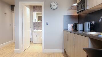 A modern kitchen with wooden cabinets, a built-in microwave, and a sink. There is a clock on the wall and a door leading to another room.