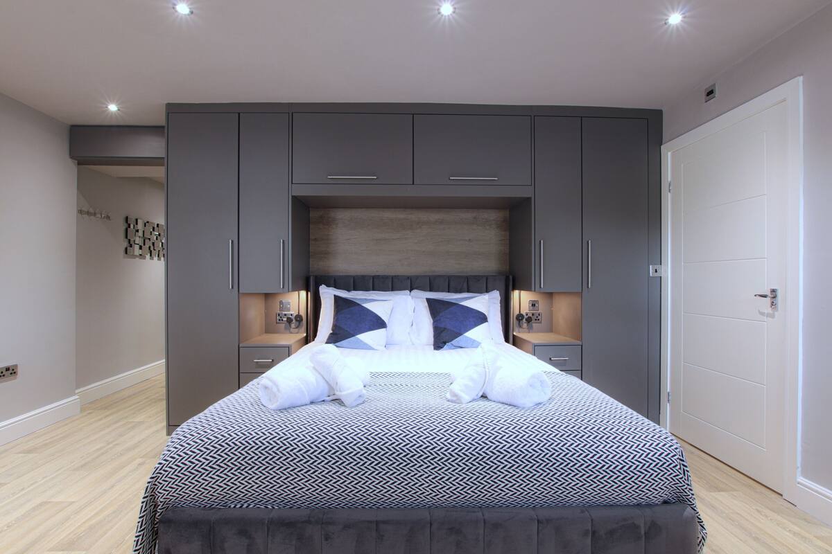A modern bedroom with a large bed, grey cabinets, and bedside lamps.