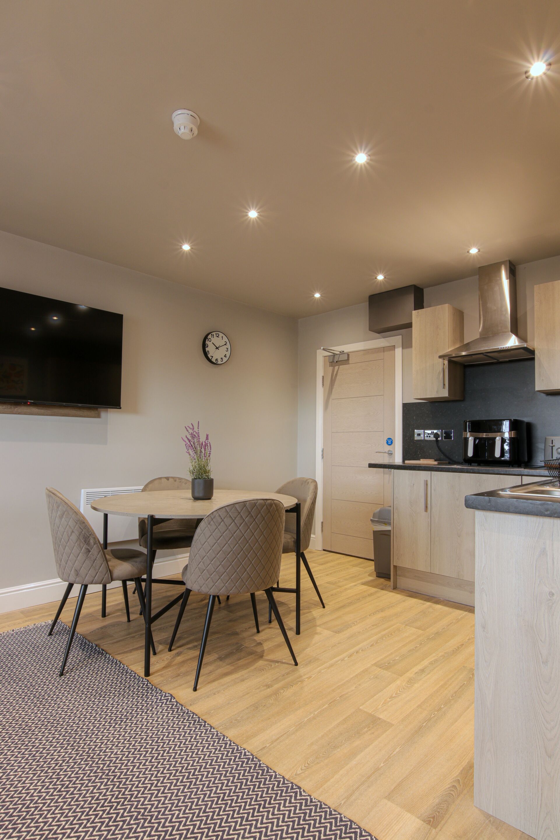 A modern kitchen with a dining area, a flat-screen TV, and a clock on the wall.