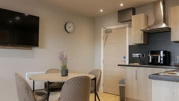 A modern kitchen with a dining area, a flat-screen TV, and a clock on the wall.