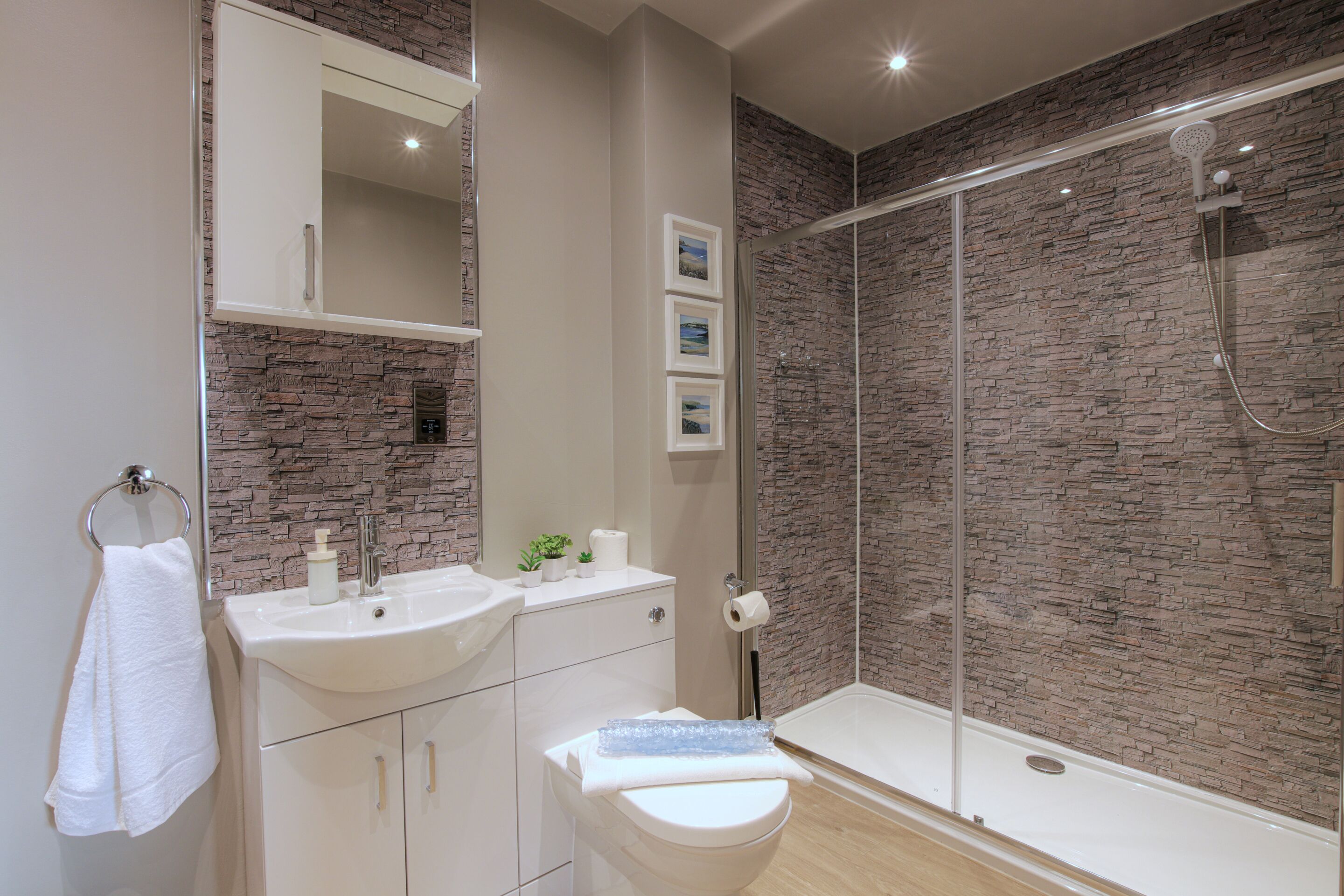 Een moderne badkamer met een wand met een steenstructuur, een wit wastafelmeubel en een douche met glazen wanden.