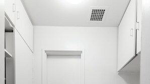 Une petite cuisine étroite avec des meubles blancs, une porte blanche, une cuisinière et un lave-vaisselle.