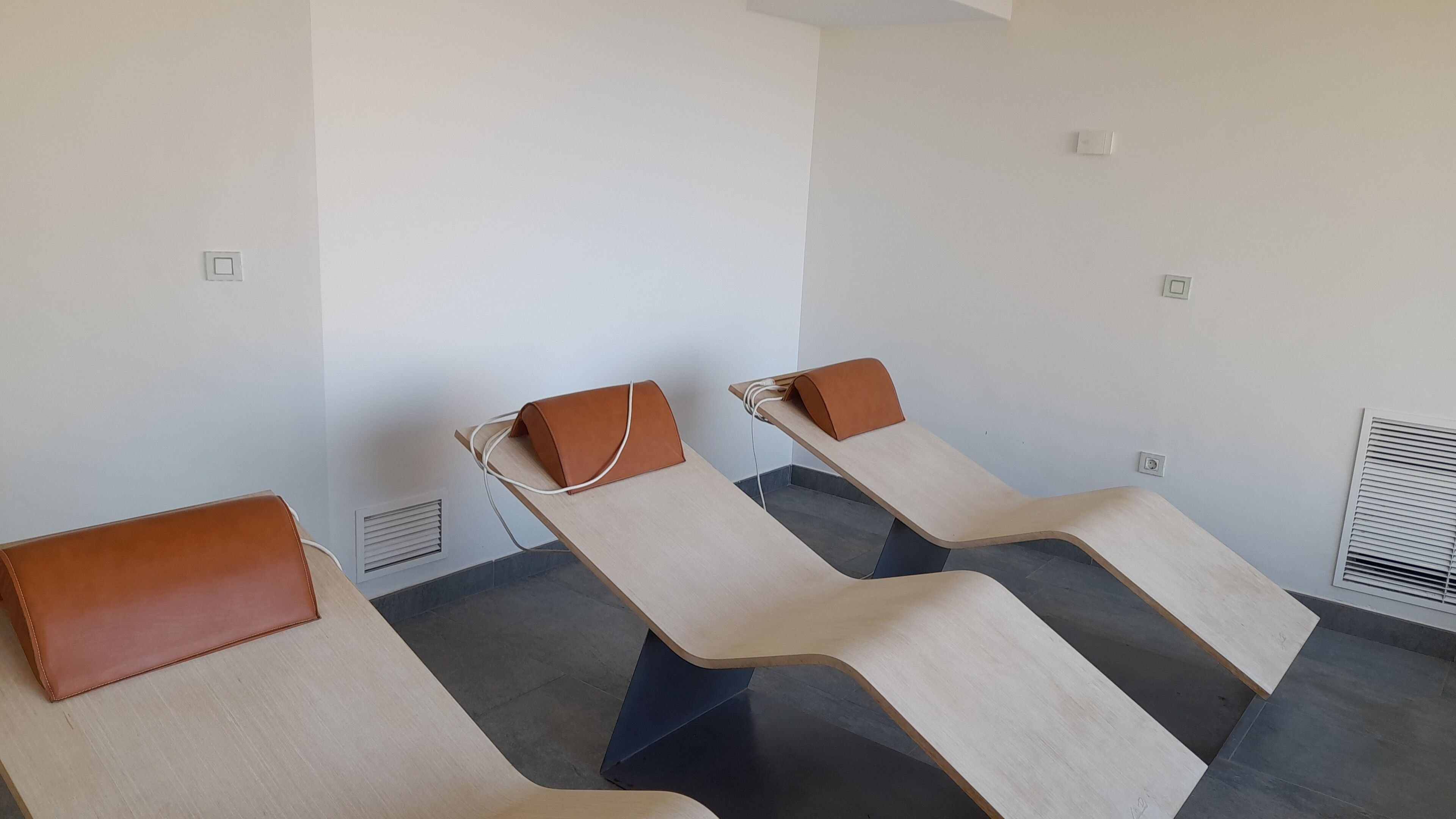 A room with three reclining chairs, each with a brown headrest, against a white wall.
