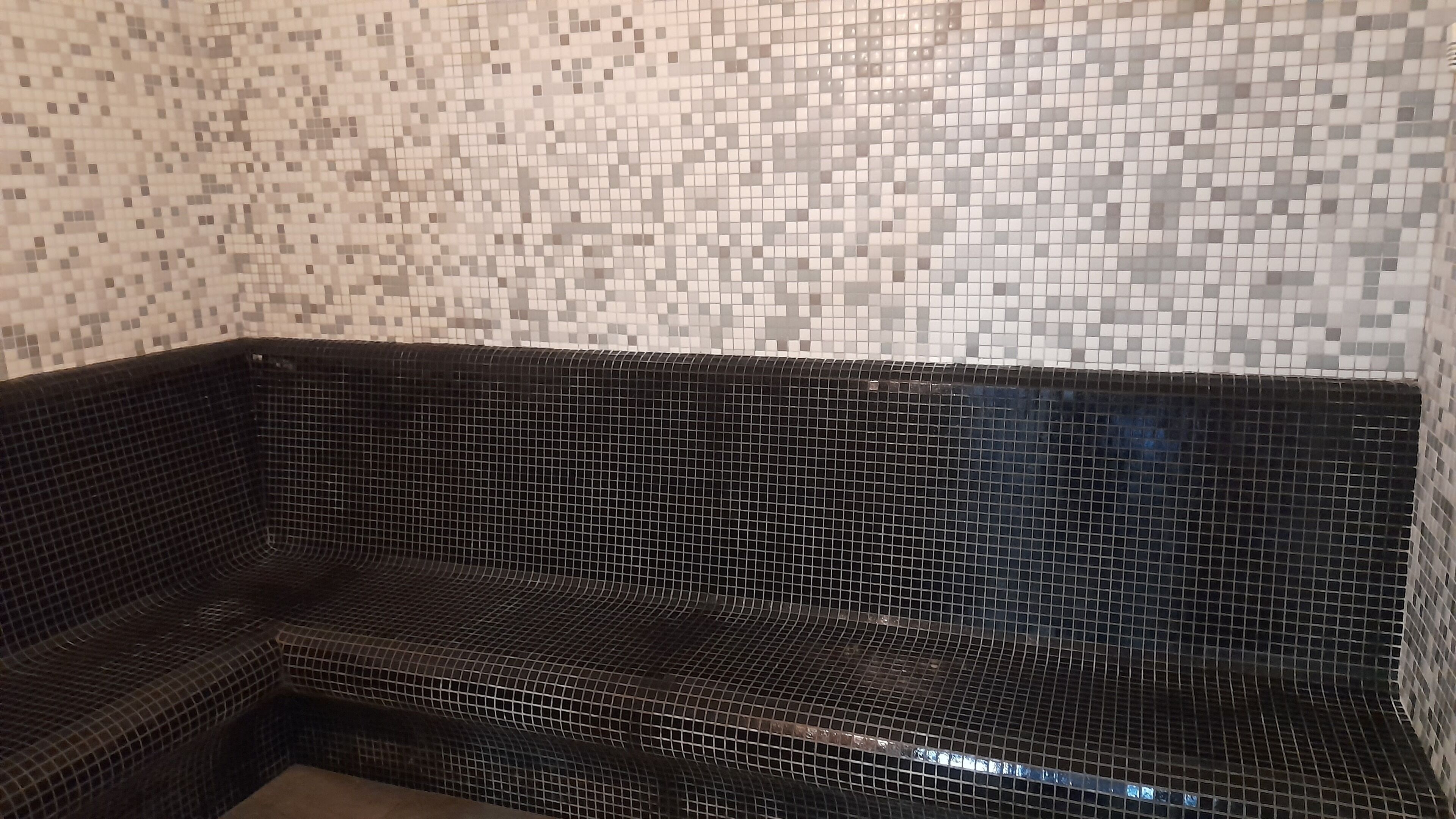 Una esquina de una habitación con un banco de baldosas negras y una pared de mosaicos.