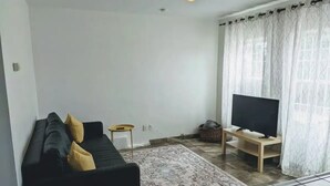 Una sala de estar con un sofá negro, una mesita de madera, un televisor sobre un mueble bajo y una alfombra estampada.