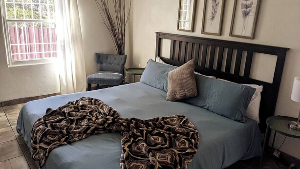 Una cama bien hecha con un edredón estampado, un cabecero oscuro y una mesita de noche con una lámpara.