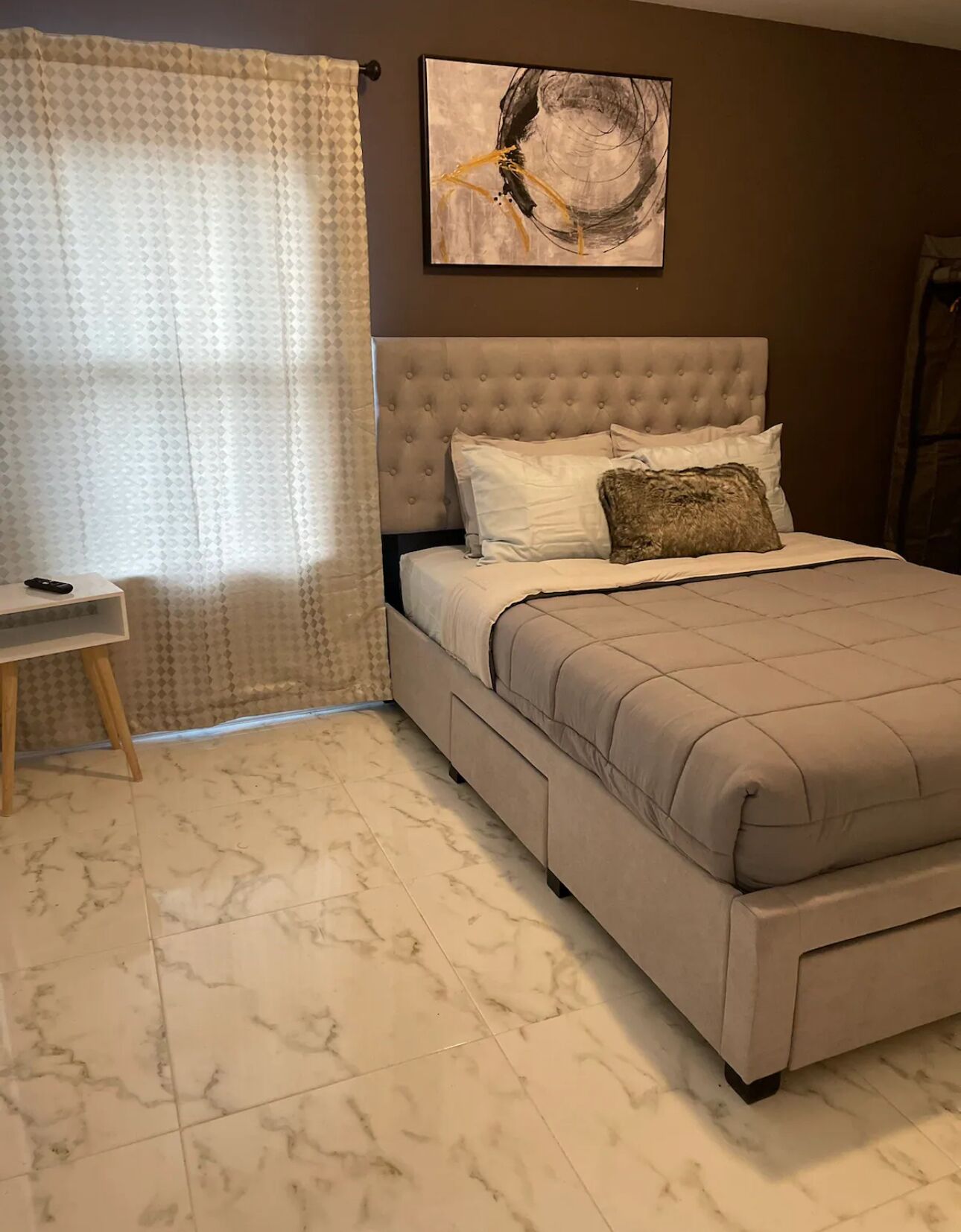 Un dormitorio con una cama de cabecera capitonada, una mesita de noche, una lámpara y un cuadro en la pared.
