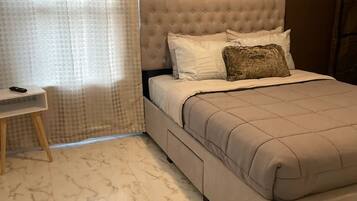 Un dormitorio con una cama de cabecera capitonada, una mesita de noche, una lámpara y un cuadro en la pared.