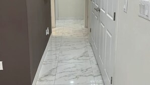 Un pasillo con suelo de mármol, paredes grises y puertas blancas.