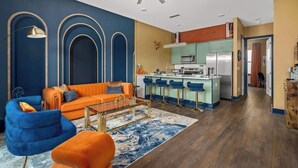 A modern living room with a sofa, ottoman, and a coffee table. There is a kitchen area with a refrigerator, microwave, and bar stools. - Chic Escape · 2mi to DT · Billiards · B-Nashy (Nashville)