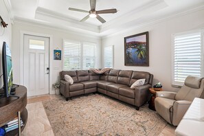 Ein Wohnzimmer mit Ecksofa, Deckenventilator, Gemälde und Fernseher.