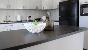 Une cuisine moderne avec des meubles blancs, un réfrigérateur noir et un plan de travail en marbre.
