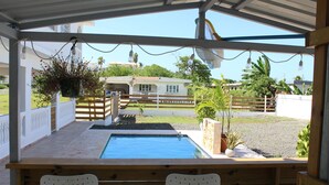 Un espace extérieur abrité avec une piscine, deux chaises en plastique blanches et un banc en bois.