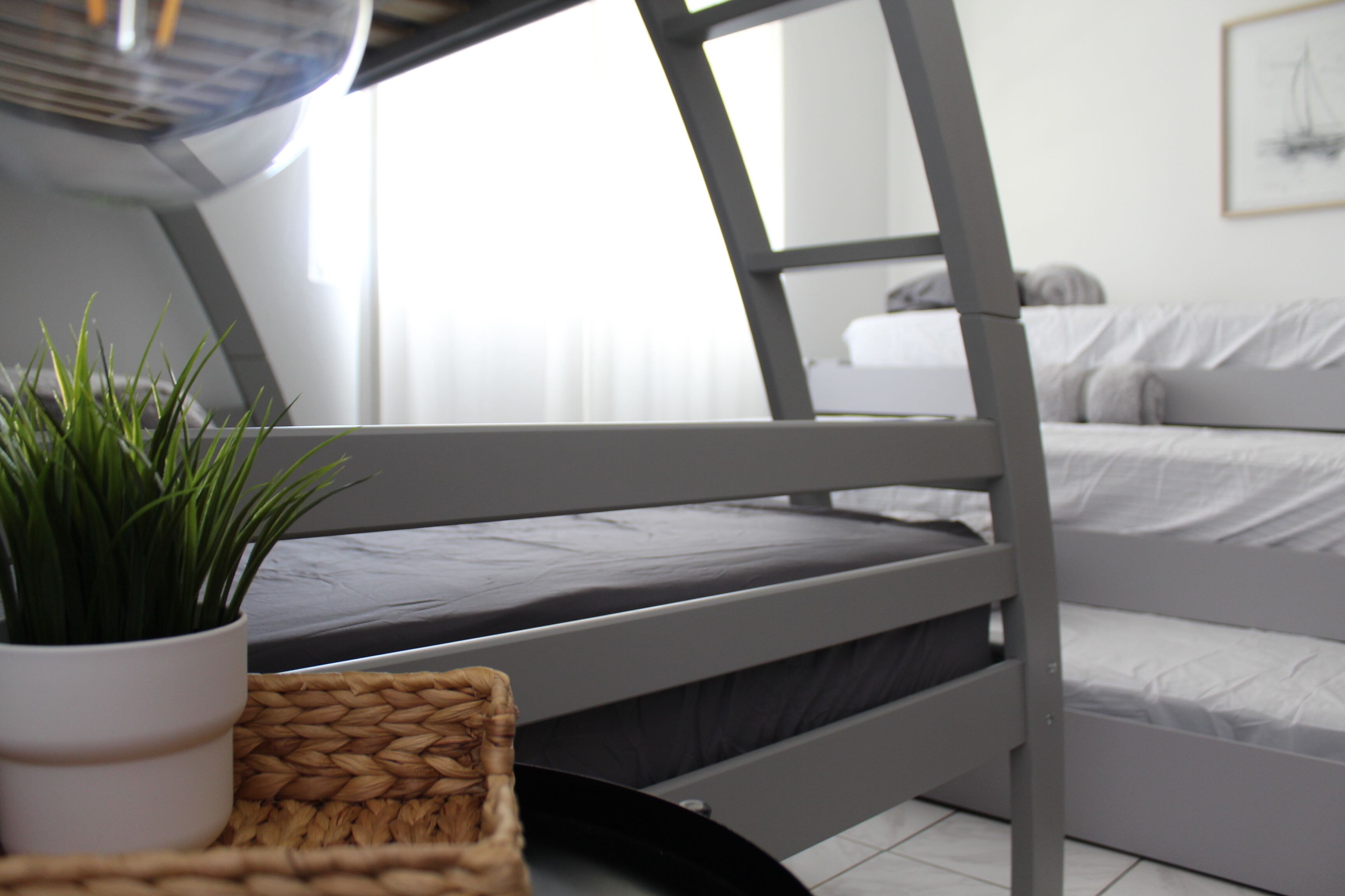 Un lit superposé avec une plante en pot et un panier tressé posés sur le sol.