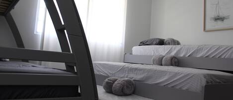 A room with three bunk beds, a window with sheer curtains, and a framed artwork on the wall.