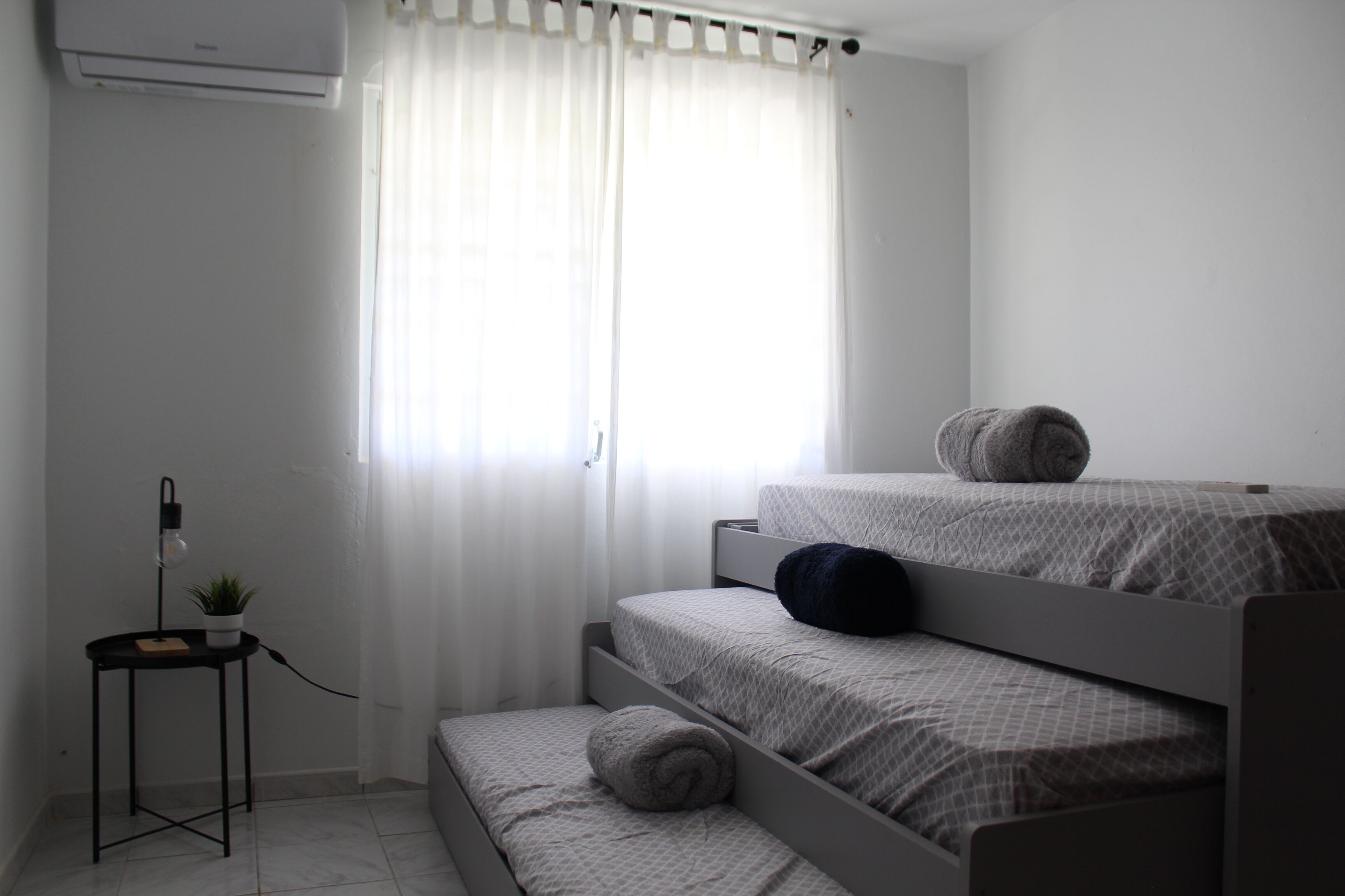 Una habitación pequeña y limpia con una cama individual doble, una mesita de noche con lámpara y una planta en maceta.