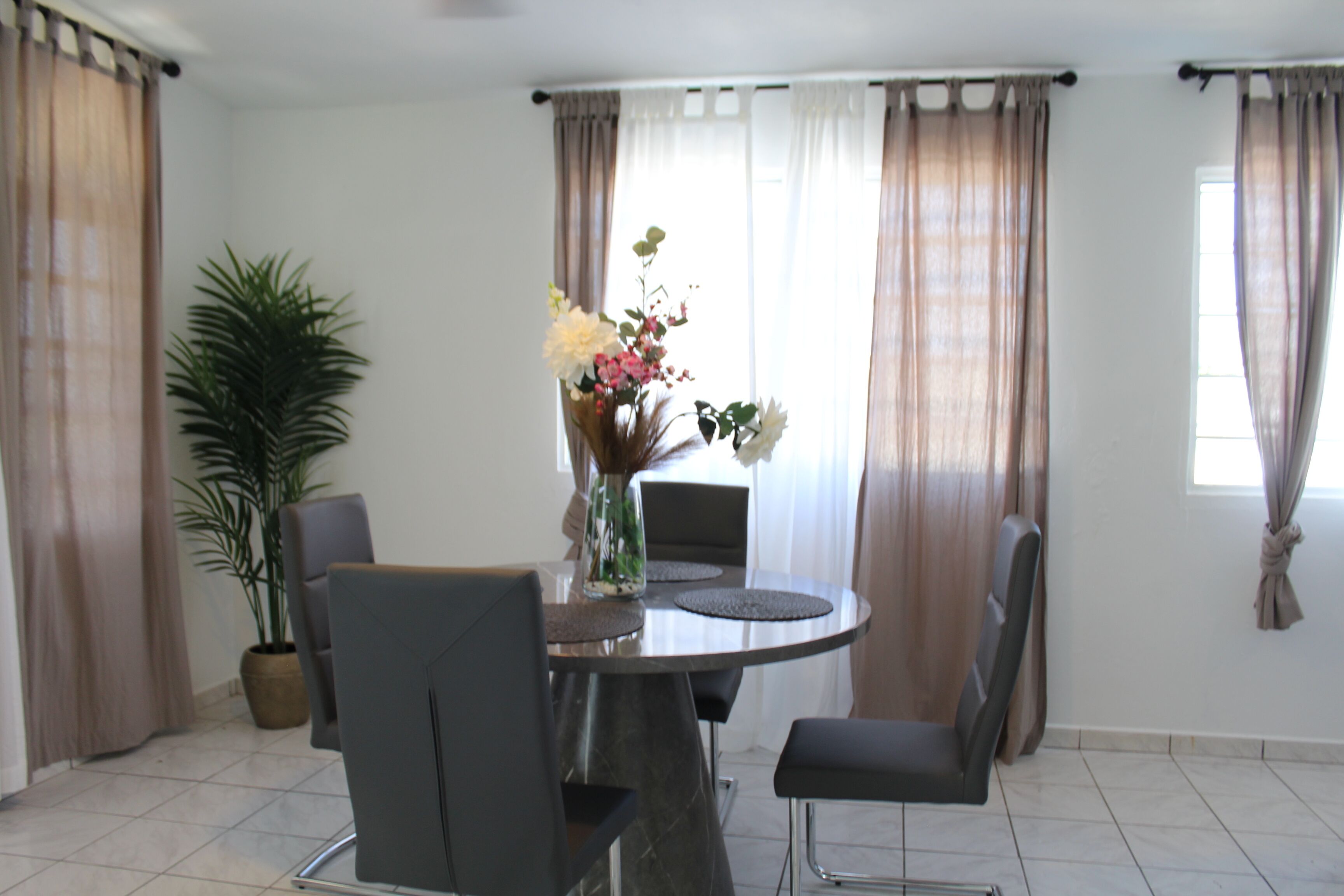 A dining area with a round table, four chairs, a vase with flowers, and a potted plant.