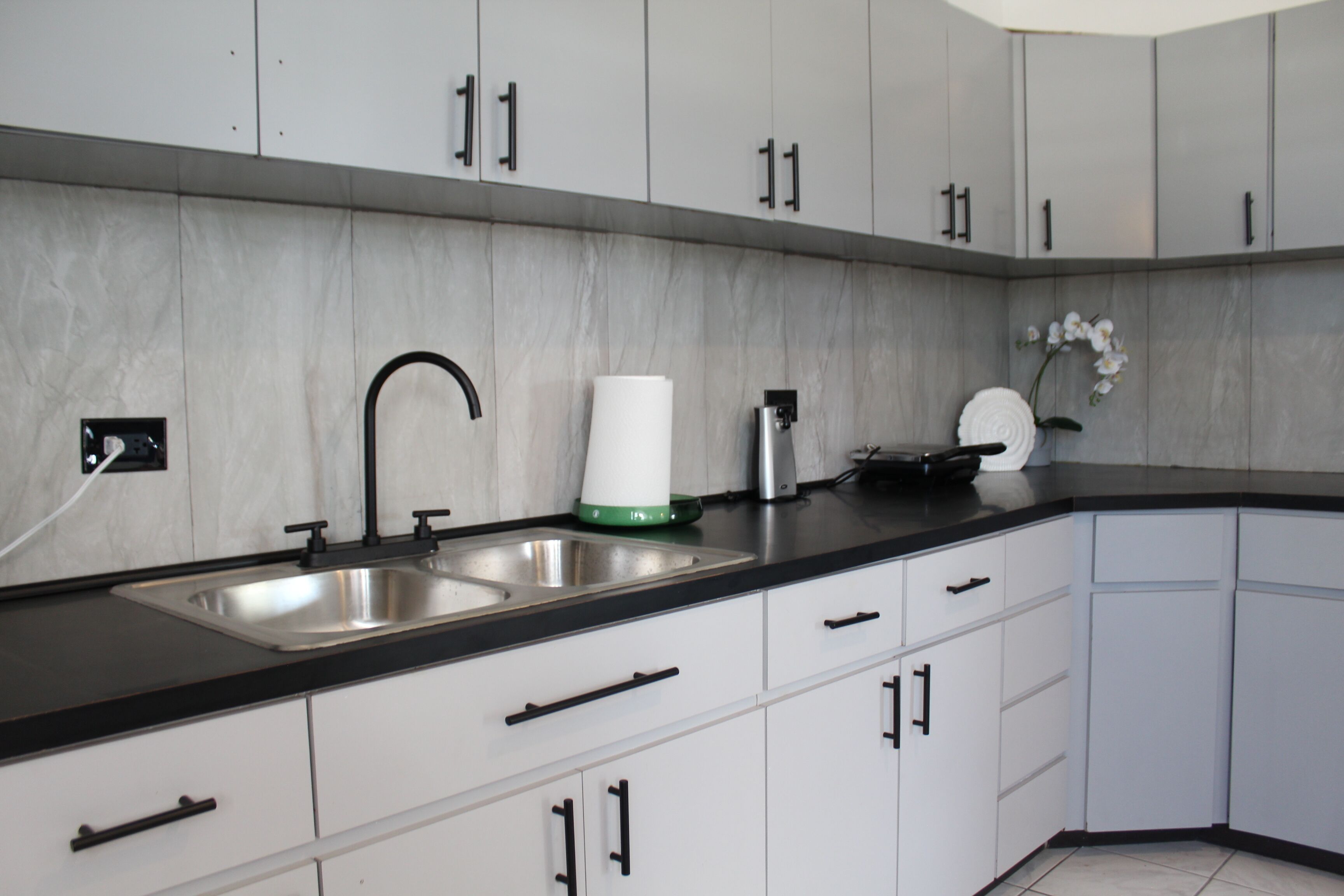 Una cocina moderna con armarios blancos, encimeras negras y electrodomésticos de acero inoxidable.