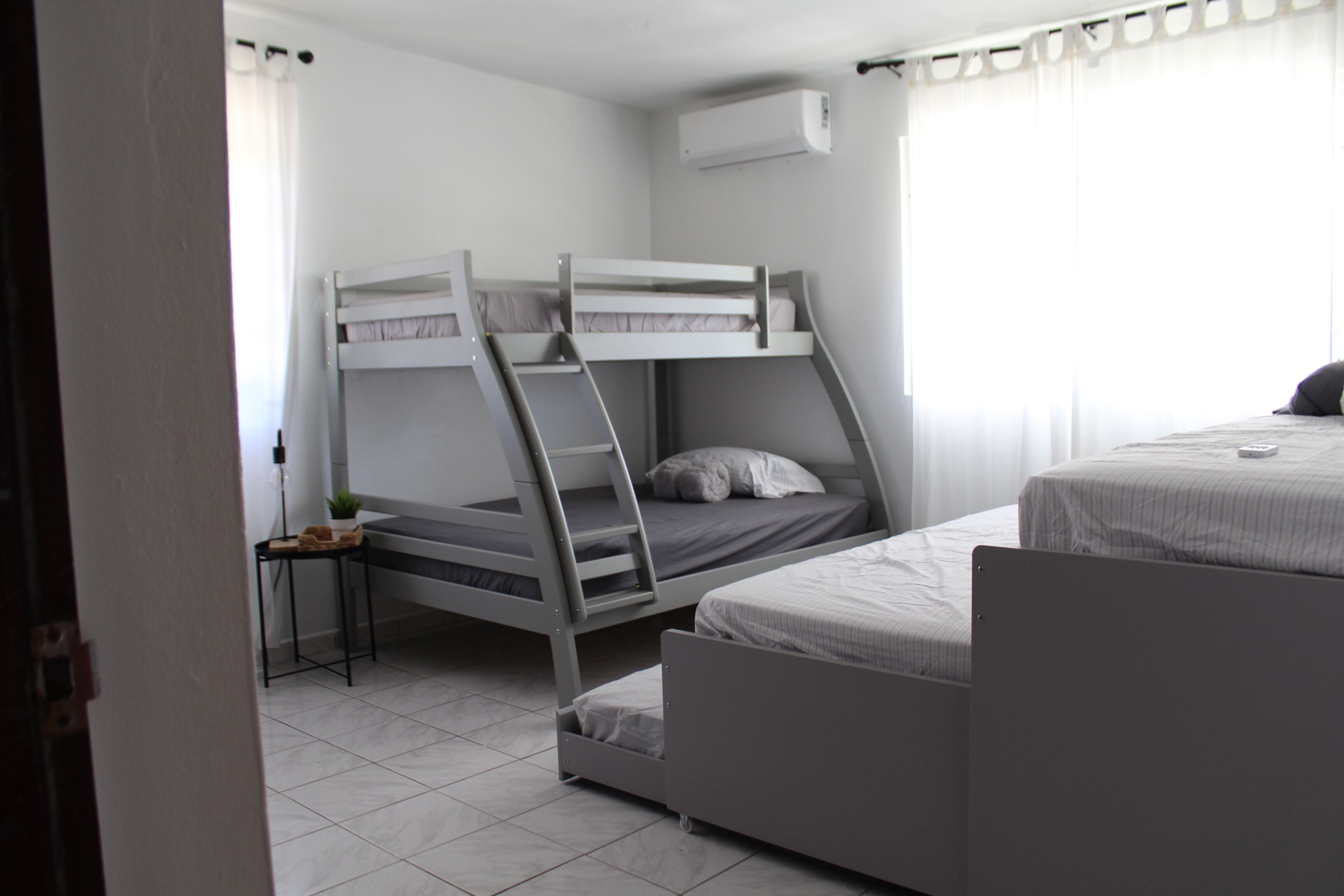 Ein Zimmer mit Etagenbetten, einem kleinen Tisch mit einer Pflanze und einem Fenster mit Vorhängen.
