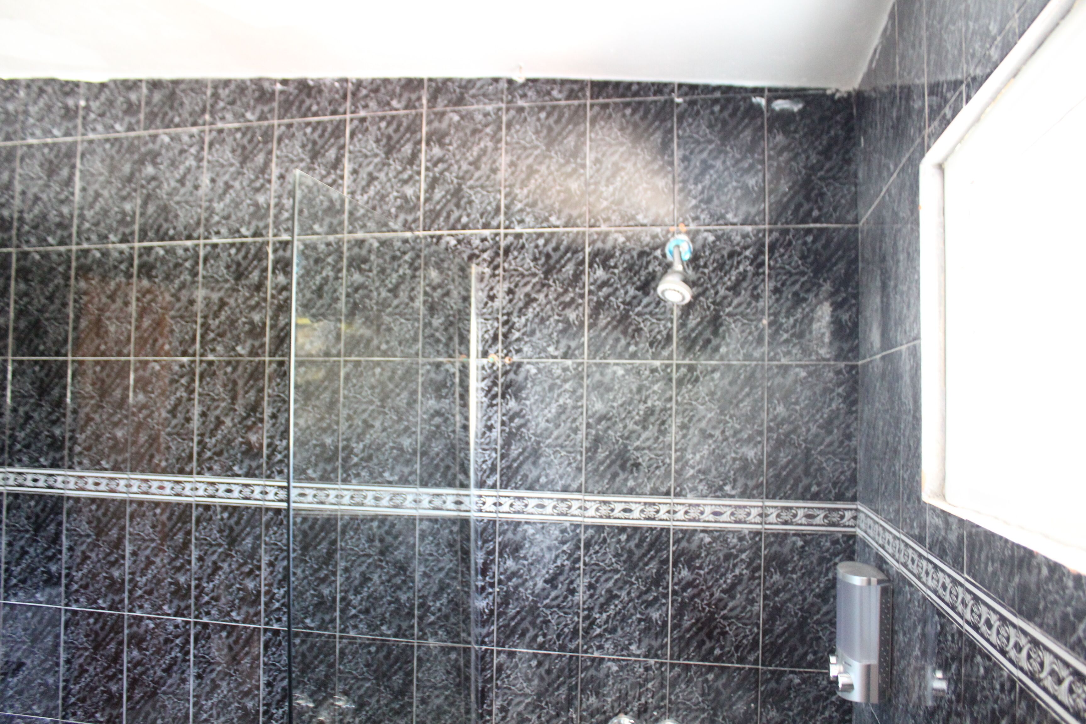 A bathroom with black marble tiles, a showerhead, and a hand dryer.