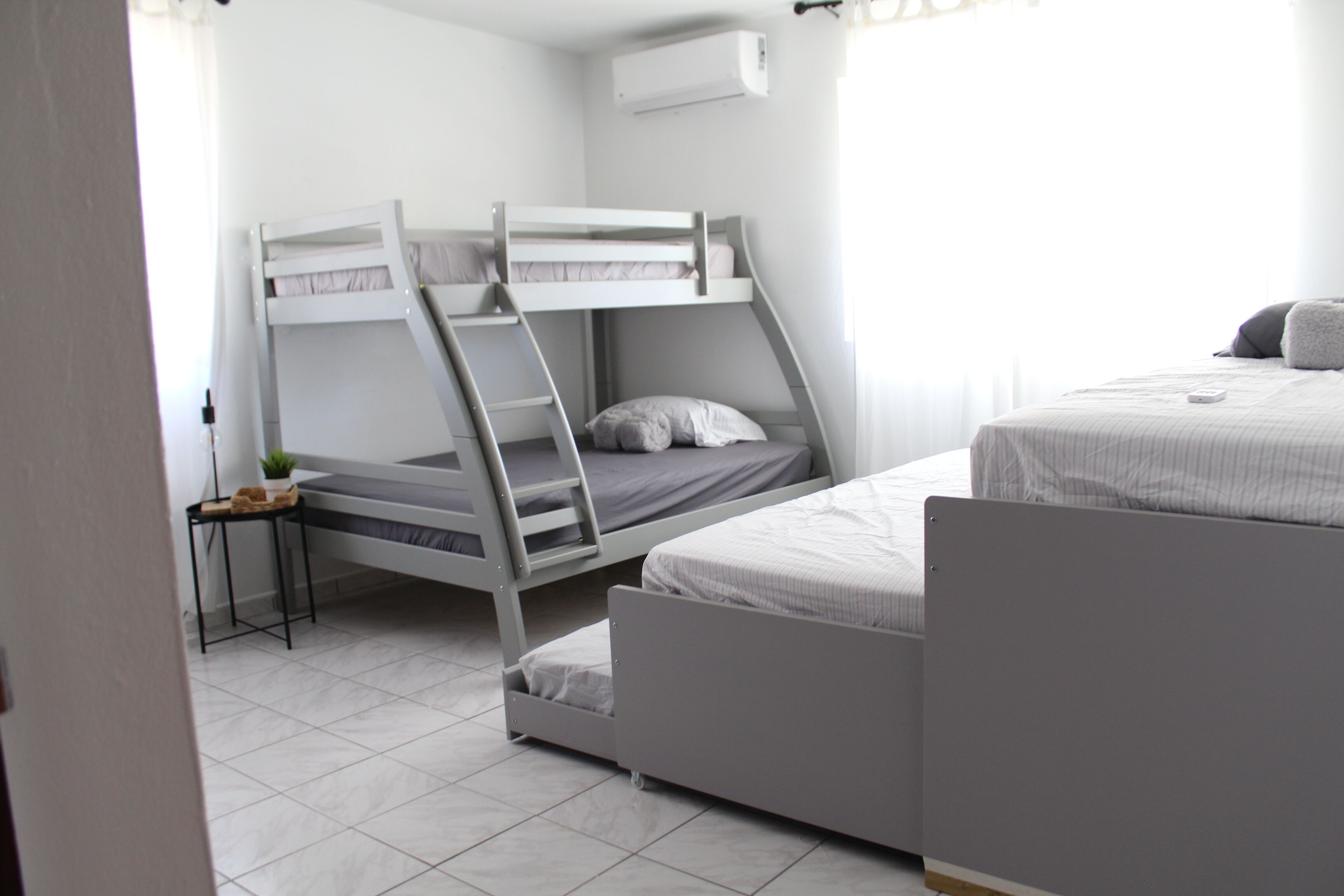 A room with bunk beds, a small table with a plant, and a window with curtains.