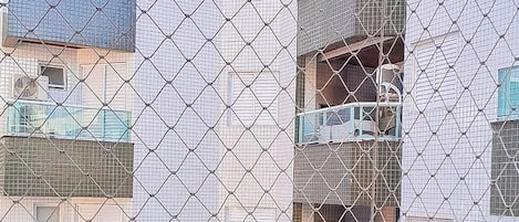 Una valla de malla metálica con barandilla de balcón, con vista a un edificio de varios pisos con balcones.
