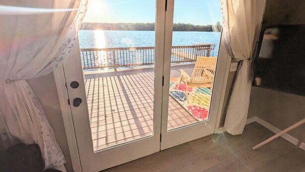 A room with a sliding glass door leading to a deck with a view of a body of water. - Lakefront Home with Sunsets, Dock, and Deck!  Dogs Stay Free! (Delton)