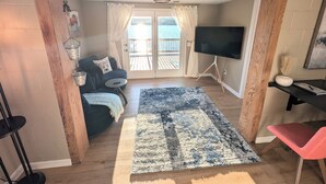 A living room with a sofa, a TV, a rug, and a view to the outside. - Lakefront Home with Sunsets, Dock, and Deck!  Dogs Stay Free! (Delton)