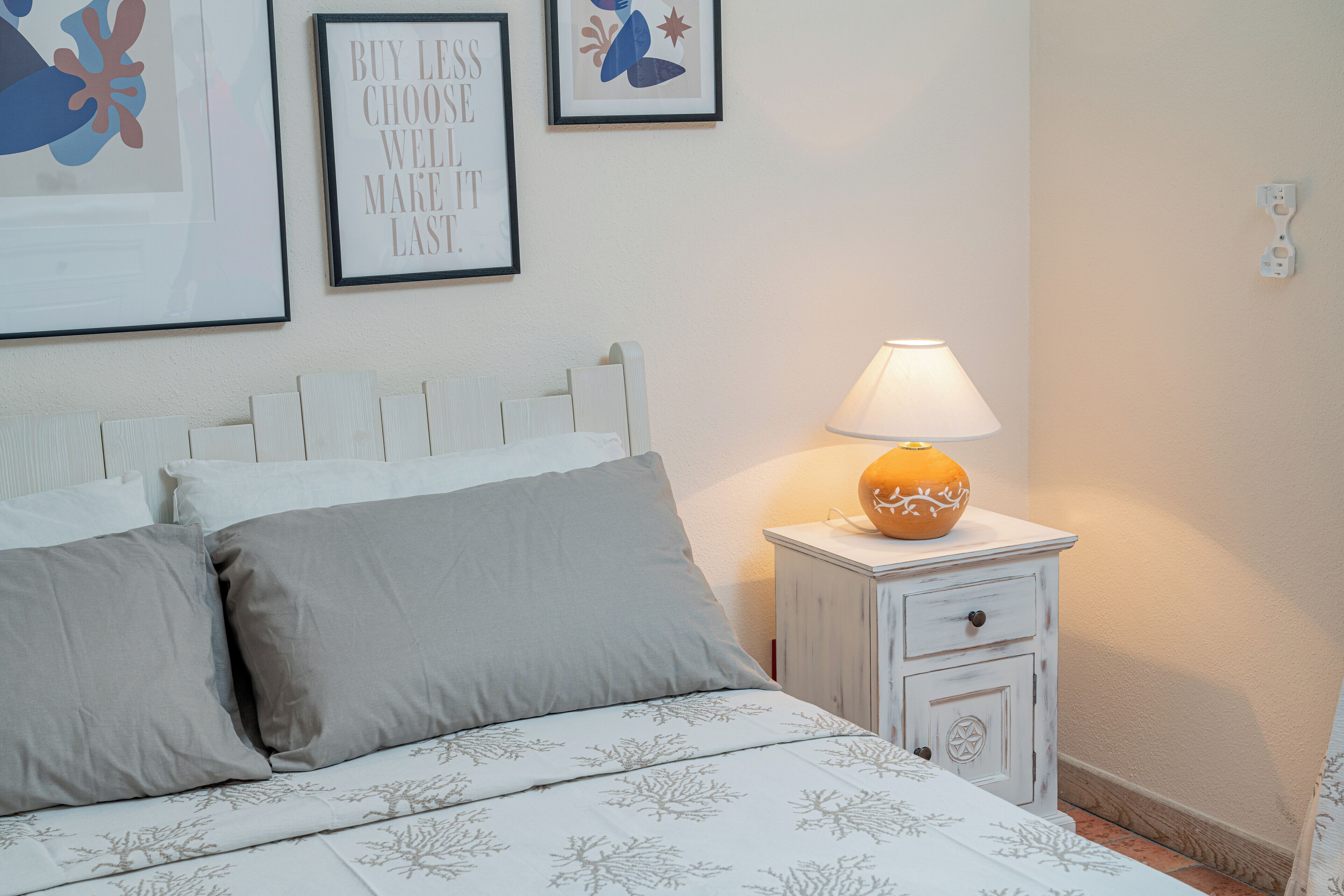 A neatly made bed with grey and white bedding, a bedside table with a lamp, and two framed motivational posters on the wall.