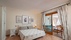 A bedroom with a bed, bedside tables, a lamp, and a view of the outside through a sliding glass door. - Sweet Mavy Incantevole Dimora by Wonderful Italy (Olbia)