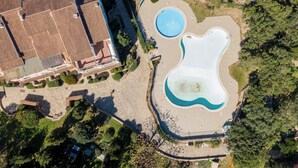 An aerial view of a swimming pool complex with multiple pools, surrounded by trees and a building with a tiled roof. - Sweet Mavy Incantevole Dimora by Wonderful Italy (Olbia)