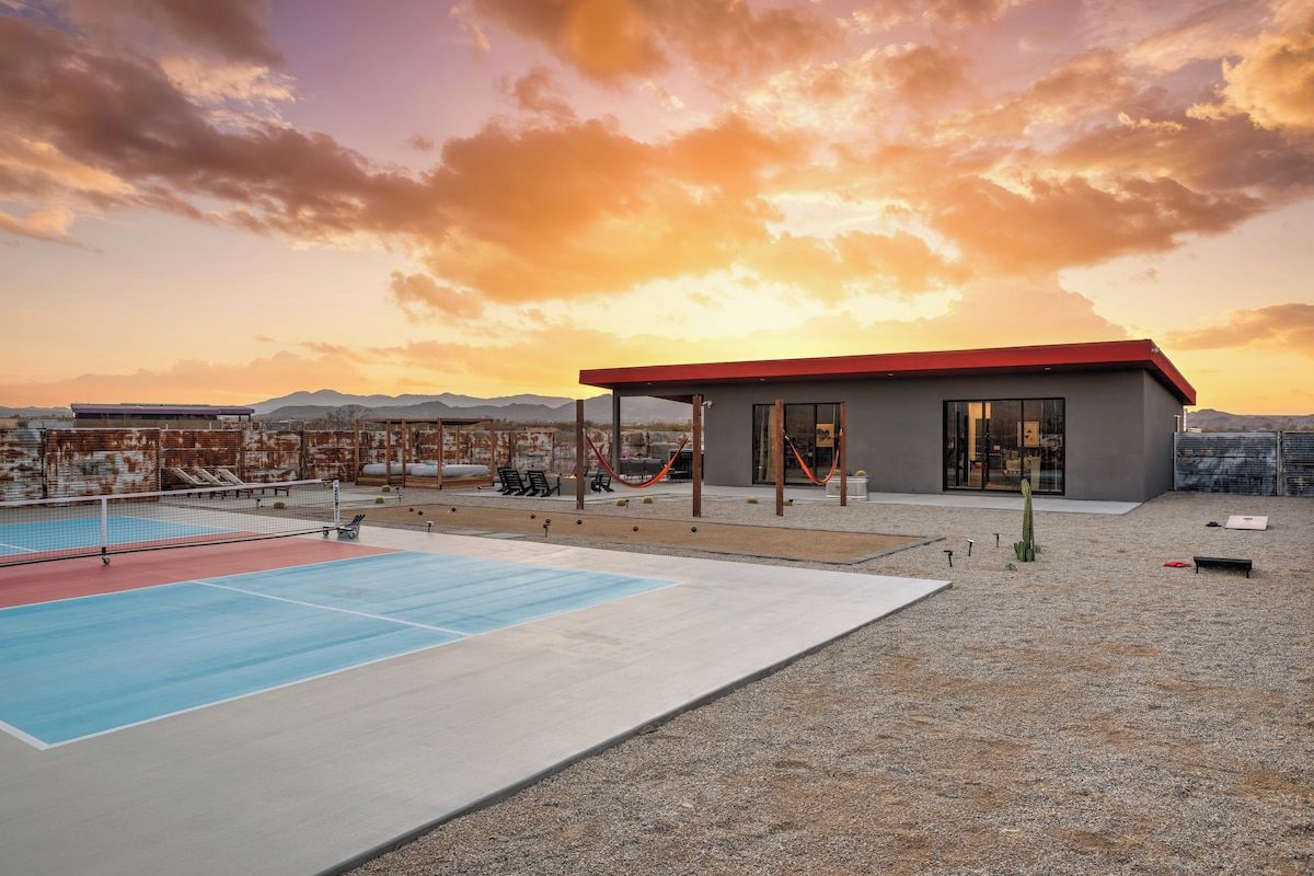 Zona d'una piscina al terrat amb una pista de tennis, cadiretes de relaxació i un edifici amb grans finestres.