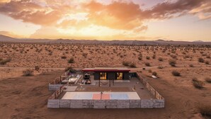 A desert landscape with a single building featuring a patio area and a view of the surrounding desert. - Joshua Tree Oasis • Pickleball • Pool • Jacuzzi (Joshua Tree)