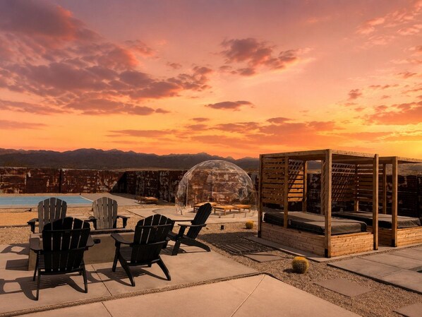 An outdoor seating area with Adirondack chairs, a wooden pergola, and a transparent dome structure.