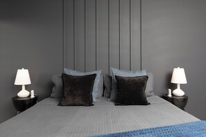 Un lit avec une tête de lit, deux lampes de chevet et un plaid bleu.