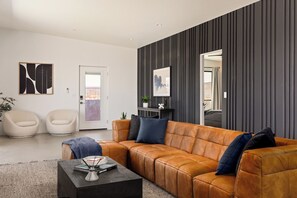 A modern living room with a leather sofa, two white chairs, a coffee table, and artwork on the walls. - Joshua Tree Oasis • Pickleball • Pool • Dome (Joshua Tree)