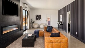 A modern living room with a fireplace, leather sofa, and a flat-screen TV. - Joshua Tree Oasis • Pickleball • Pool • Jacuzzi (Joshua Tree)