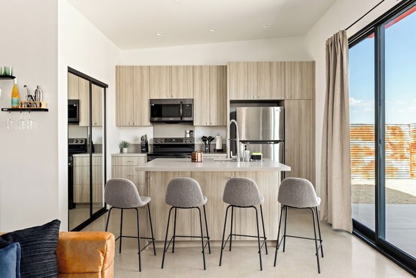 A modern kitchen with a central island, bar stools, and a large window offering a view.
