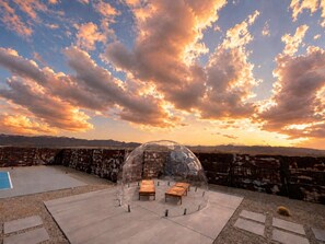 A transparent dome structure with a seating area and a pool in the background.
