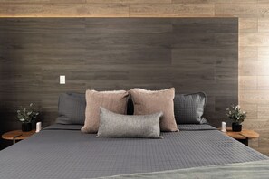 King bed with layered pillows and plush bedding against a warm wood accent wall