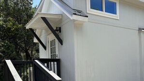 Un edificio blanco con una escalera negra que conduce a una puerta, una ventana y un pequeño espacio al aire libre con una manguera.