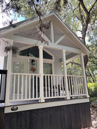 A covered porch with a white railing, a window with blinds, and a sign on the door.