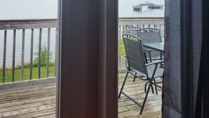 A view from a window overlooking a wooden deck with outdoor furniture, a dock, and a body of water. - Oceanside beautiful vacation property! (Lewisporte)