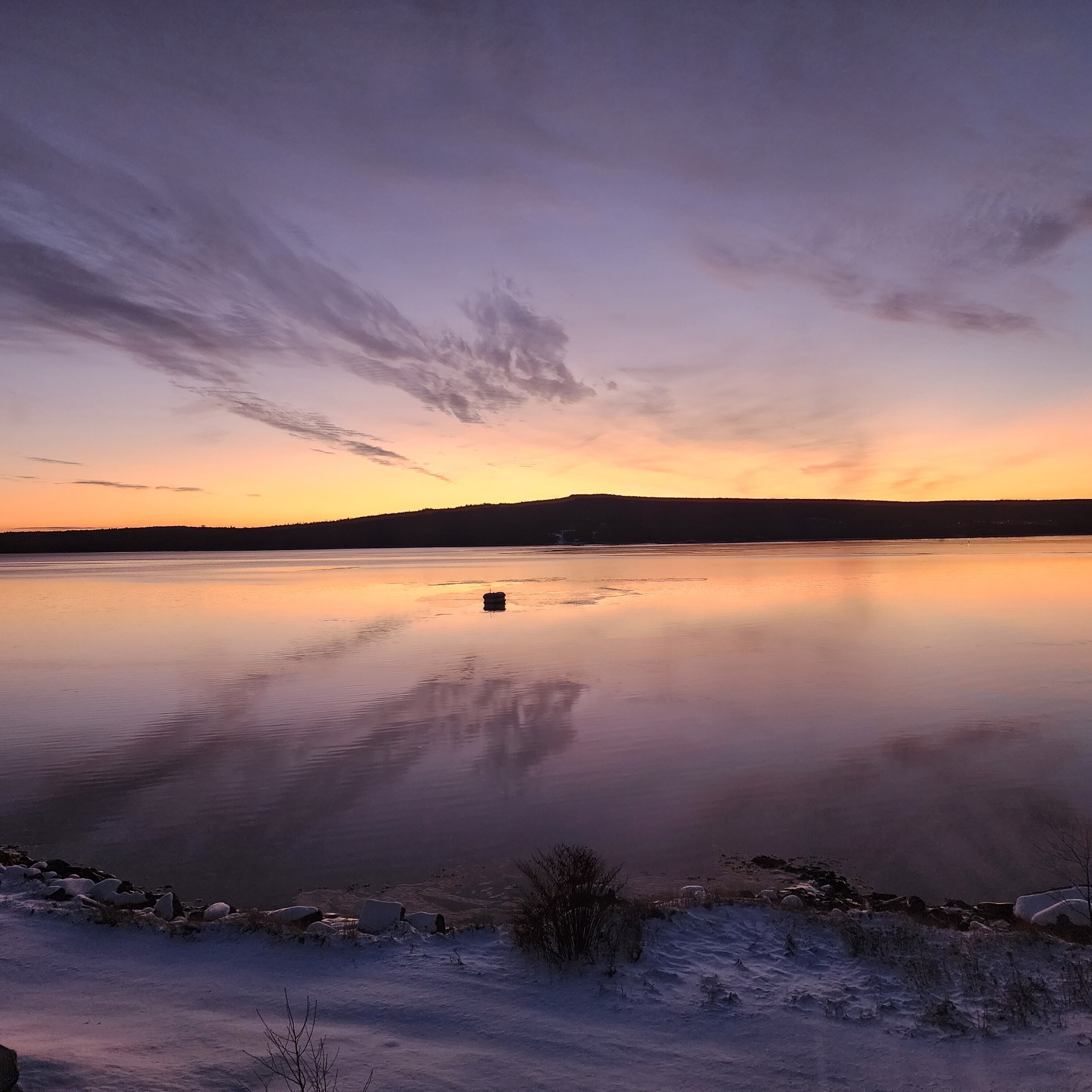 A calm lake at sunset with a clear sky and a distant shoreline.